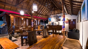 A wooden dining area with tables and chairs, a Buddha statue, and a staircase leading to an upper level.