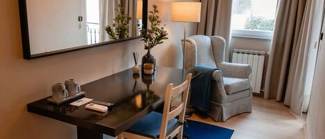 A hotel room with a desk, chair, lamp, and a large mirror.
