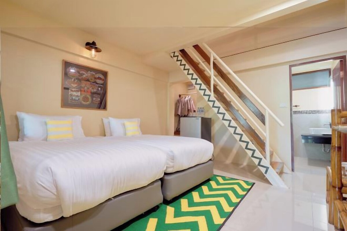 A bedroom with a bed, a staircase, and a bathroom visible in the background.