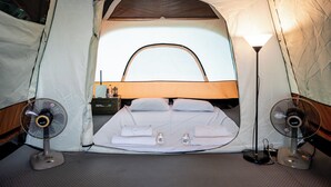 Ein Zelt mit einem Bett, zwei Ventilatoren und einer Lampe.