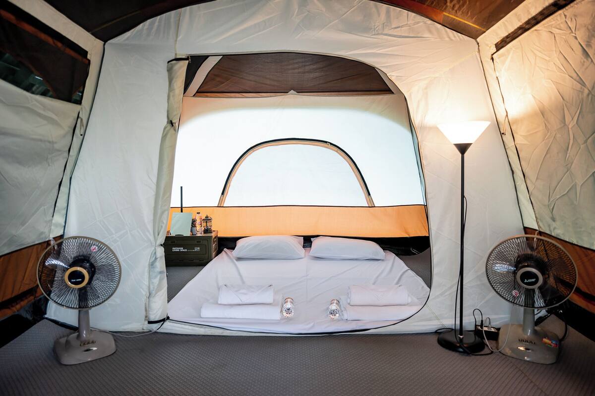 Een tent met een bed, twee ventilatoren en een lamp.