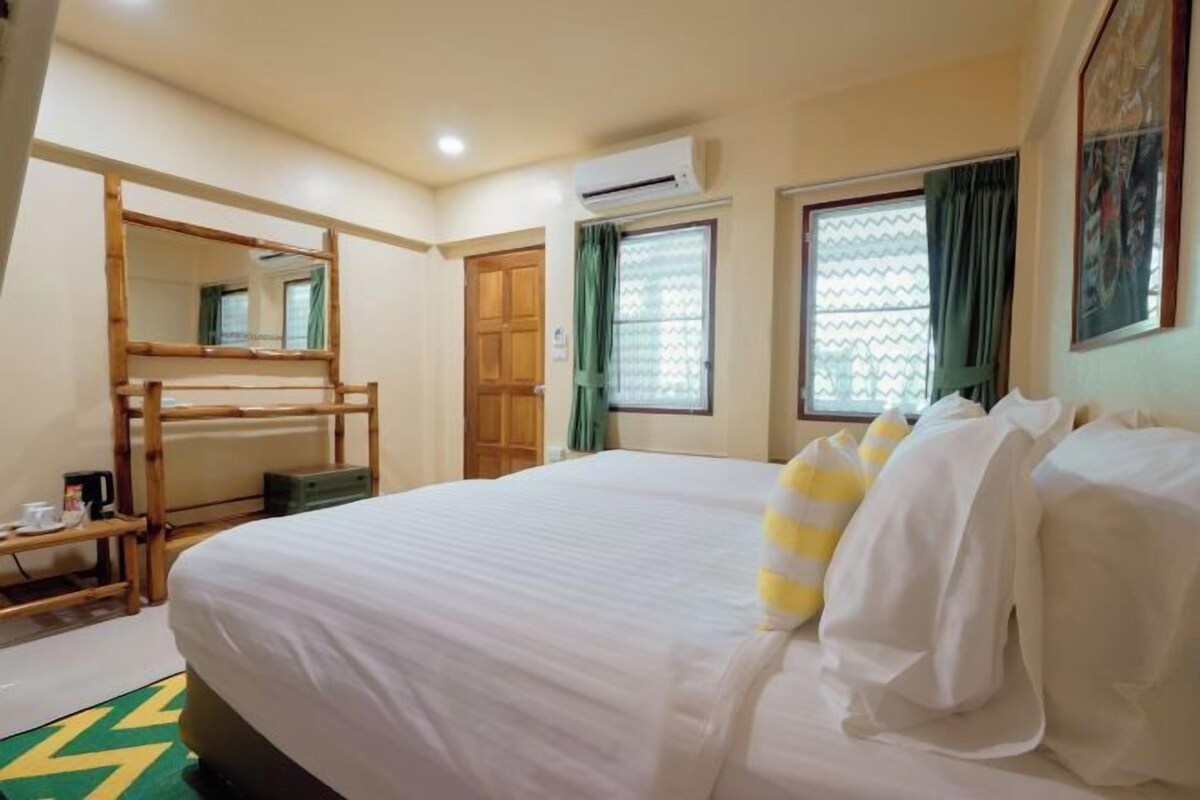 A hotel room with a bed, a wooden bunk bed, a window with curtains, an air conditioning unit, and a mirror.