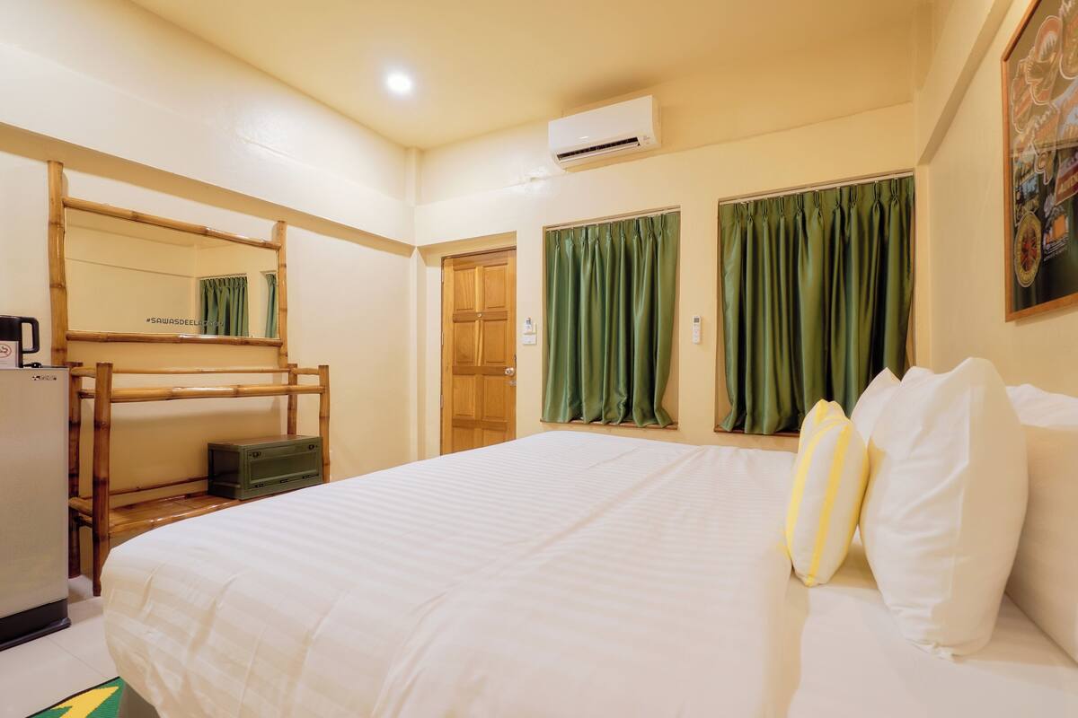 Hotelkamer met een stapelbed, een eenpersoonsbed, groene gordijnen, een wandairconditioner en een schilderij aan de muur.