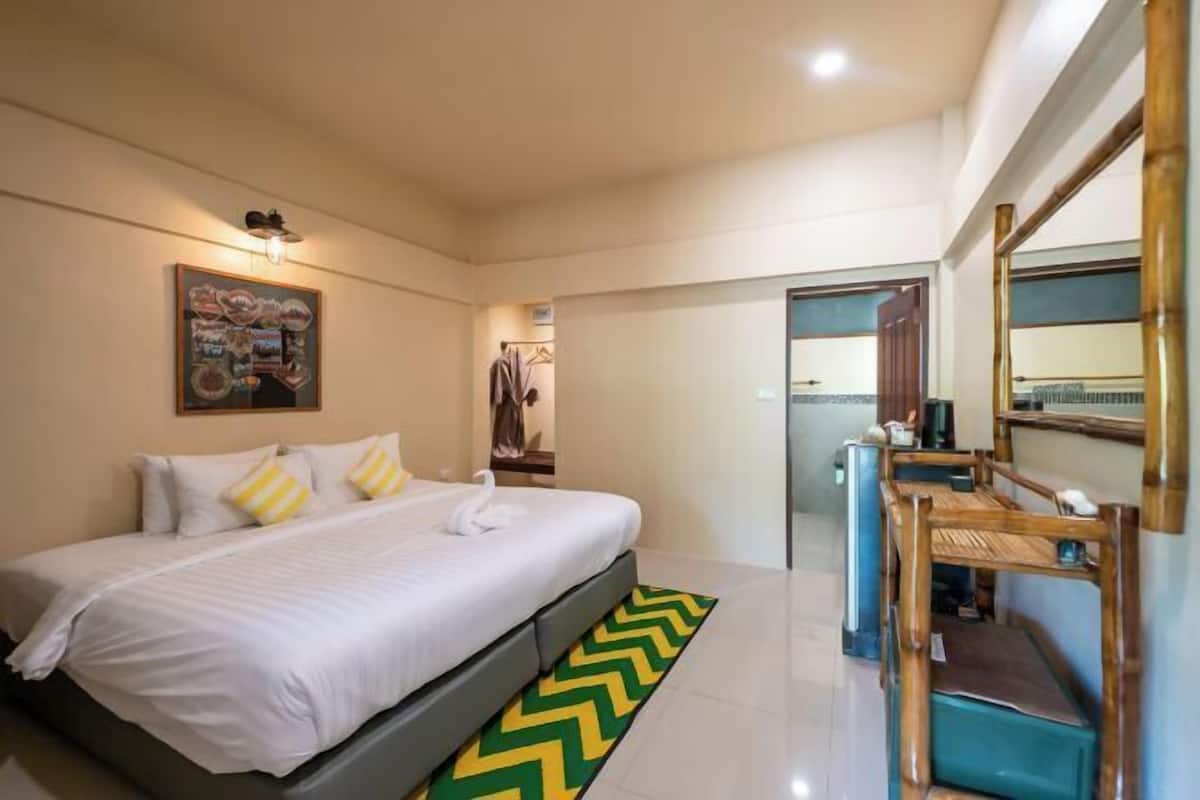 Een hotelkamer met een bed, een bureau met stoel, een spiegel en een deur naar een andere kamer.