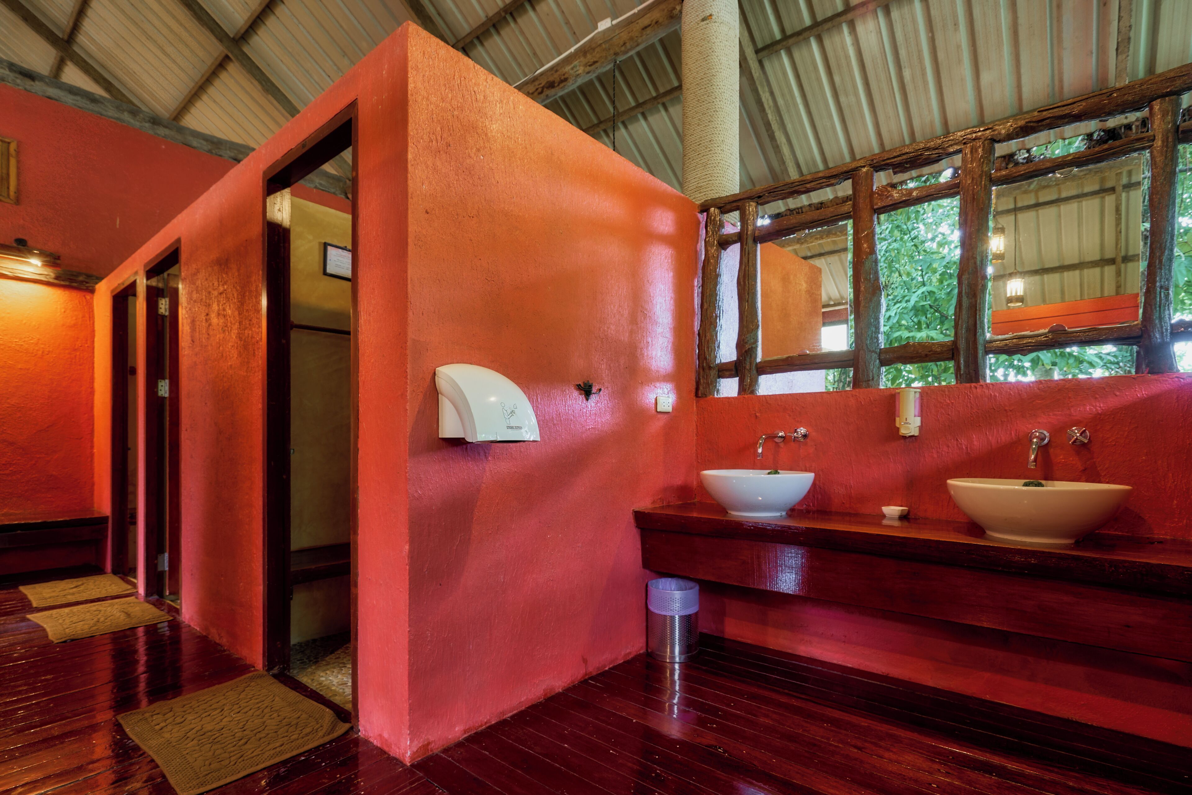 Un baño con pared roja, suelo de madera y un ventanal grande.