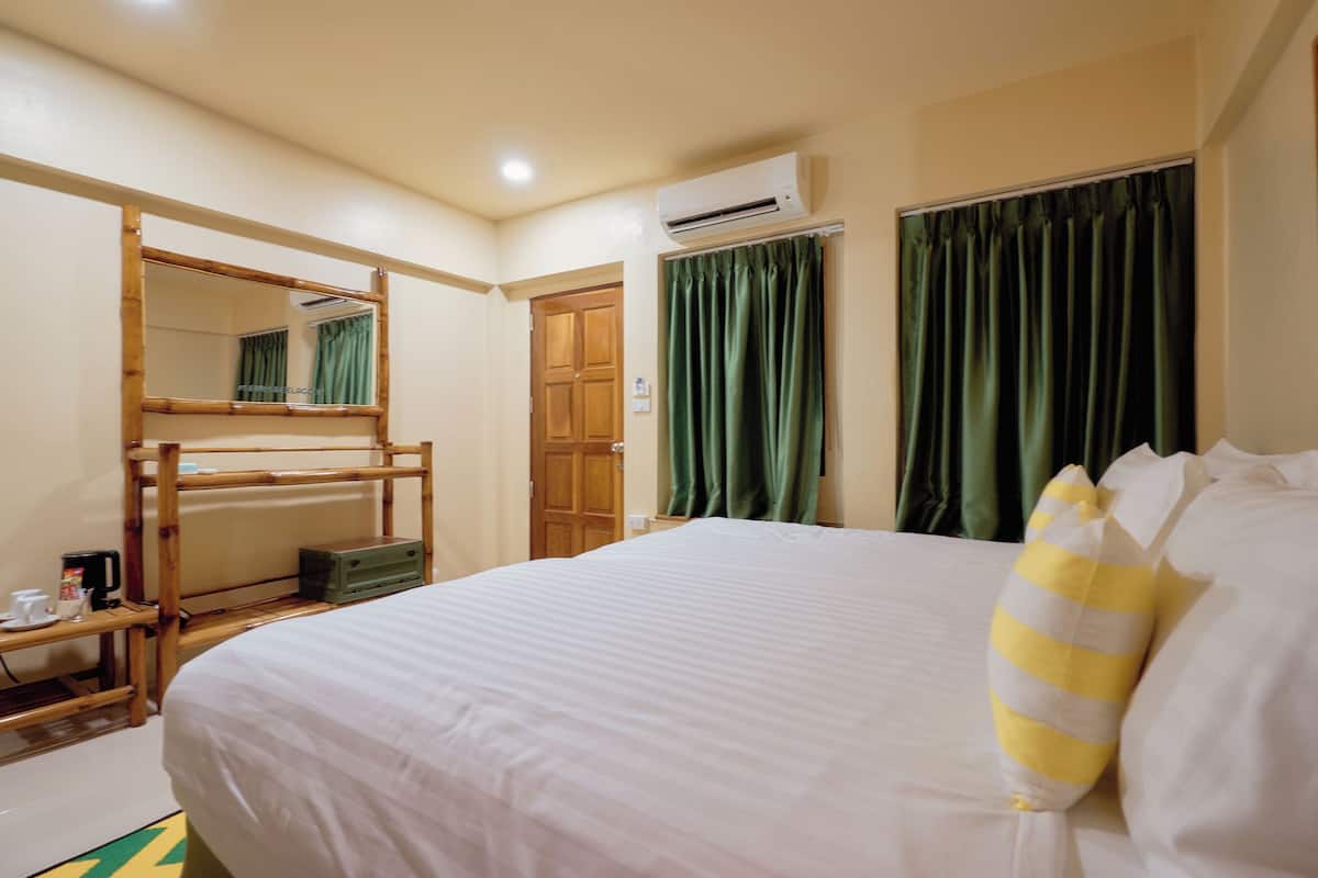 Een hotelkamer met een stapelbed, een nachtkastje met een koffiezetapparaat, een airconditioner en groene gordijnen.