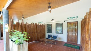 Ein Empfangsbereich mit Bambuswand, einer Rezeption, zwei Stühlen, einem Deckenventilator und einer Holztür.