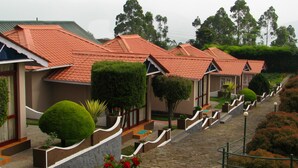 A row of uniform, single-story buildings with red-tiled roofs and a stone pathway leading between them. - Holiday Heaven Munnar (Devikolam)