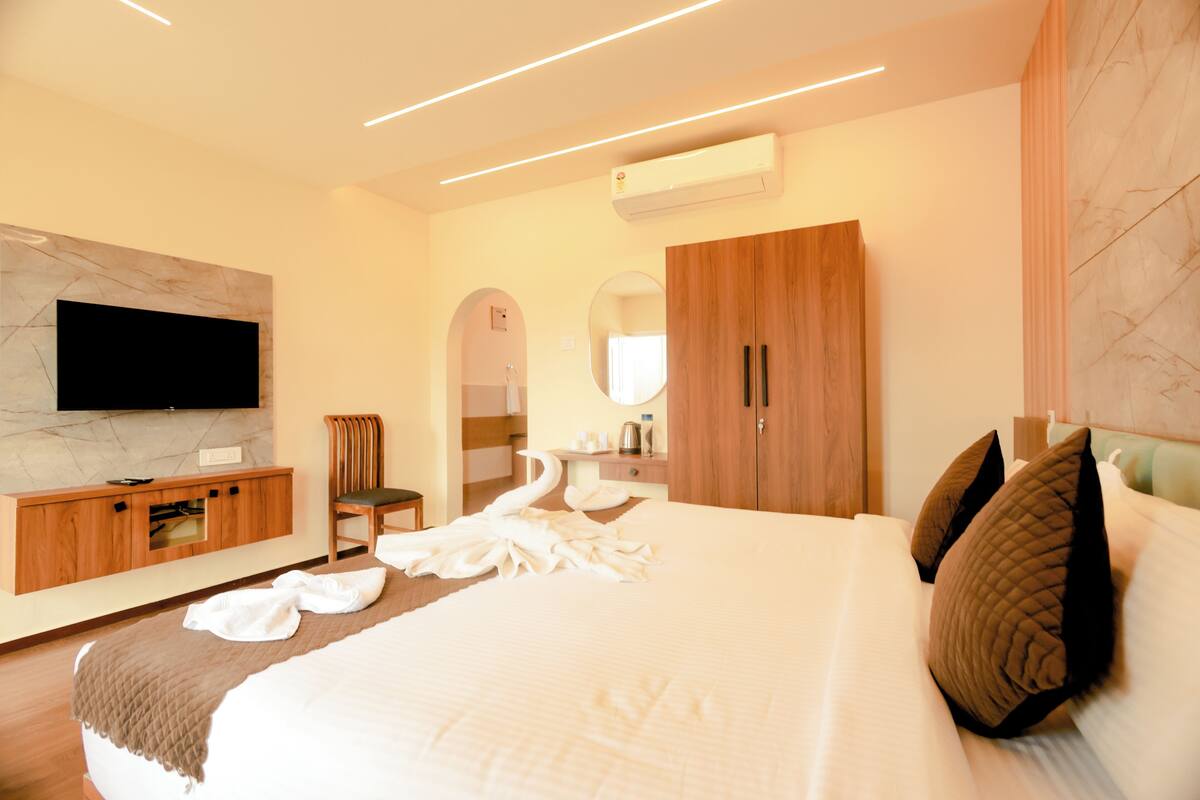 Een moderne hotelkamer met een groot bed, een flatscreen televisie aan de muur, een houten garderobe en een kaptafel met spiegel.