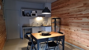 A compact kitchen with modern appliances, a dining table with chairs, and a wooden accent wall. - Place Of Moments Natur (Vila Franca do Campo)