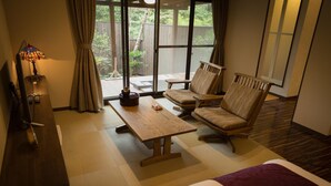 A hotel room with a bed, a wooden table, two chairs, a TV, and a window with a view of the outdoors.