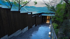 A wet stone pathway leading to a wooden gate, surrounded by lush greenery and a mountain backdrop.