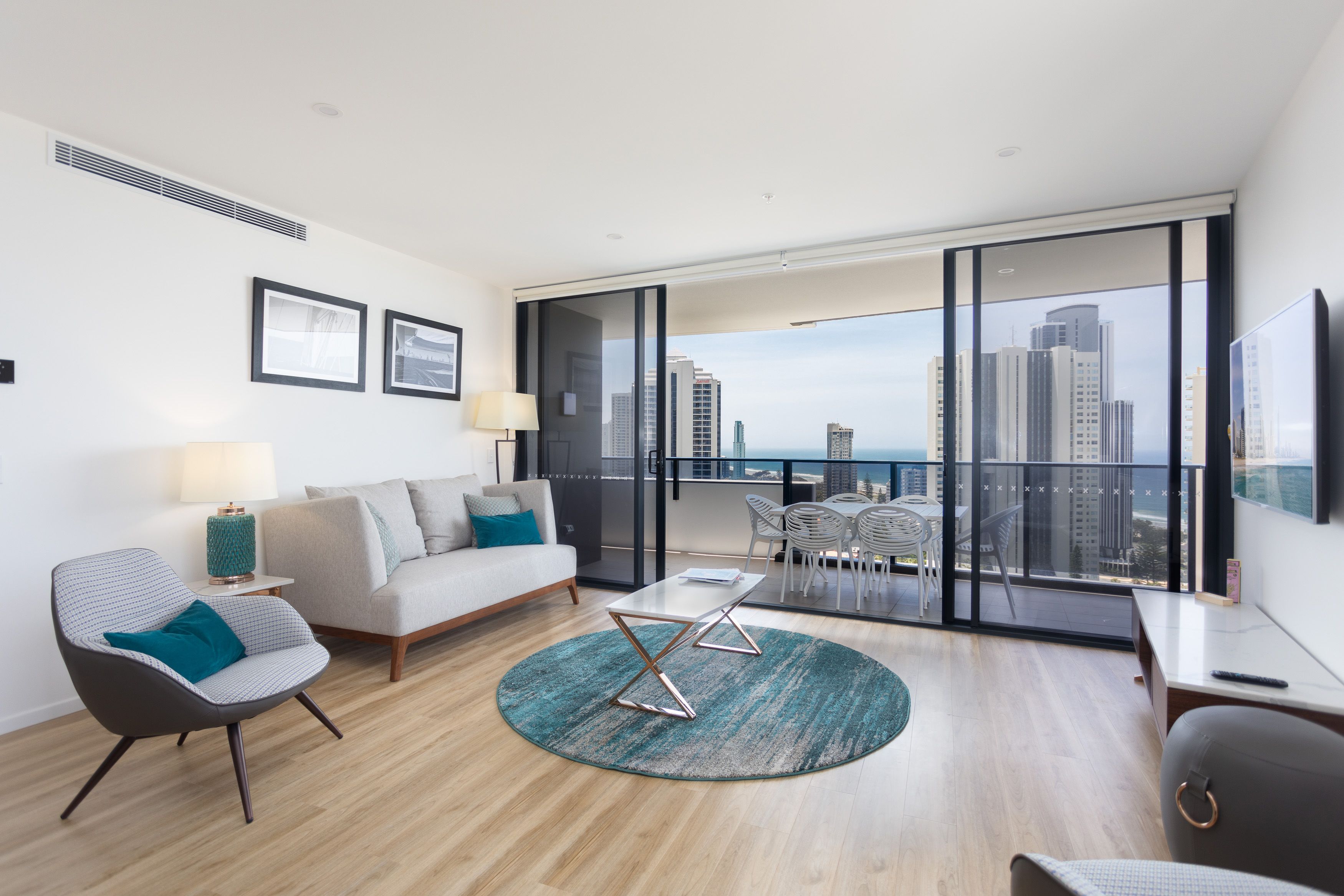 Uma sala de estar moderna com sofá, poltrona e mesa de centro, varanda com vista para a cidade e área de jantar com cadeiras.
