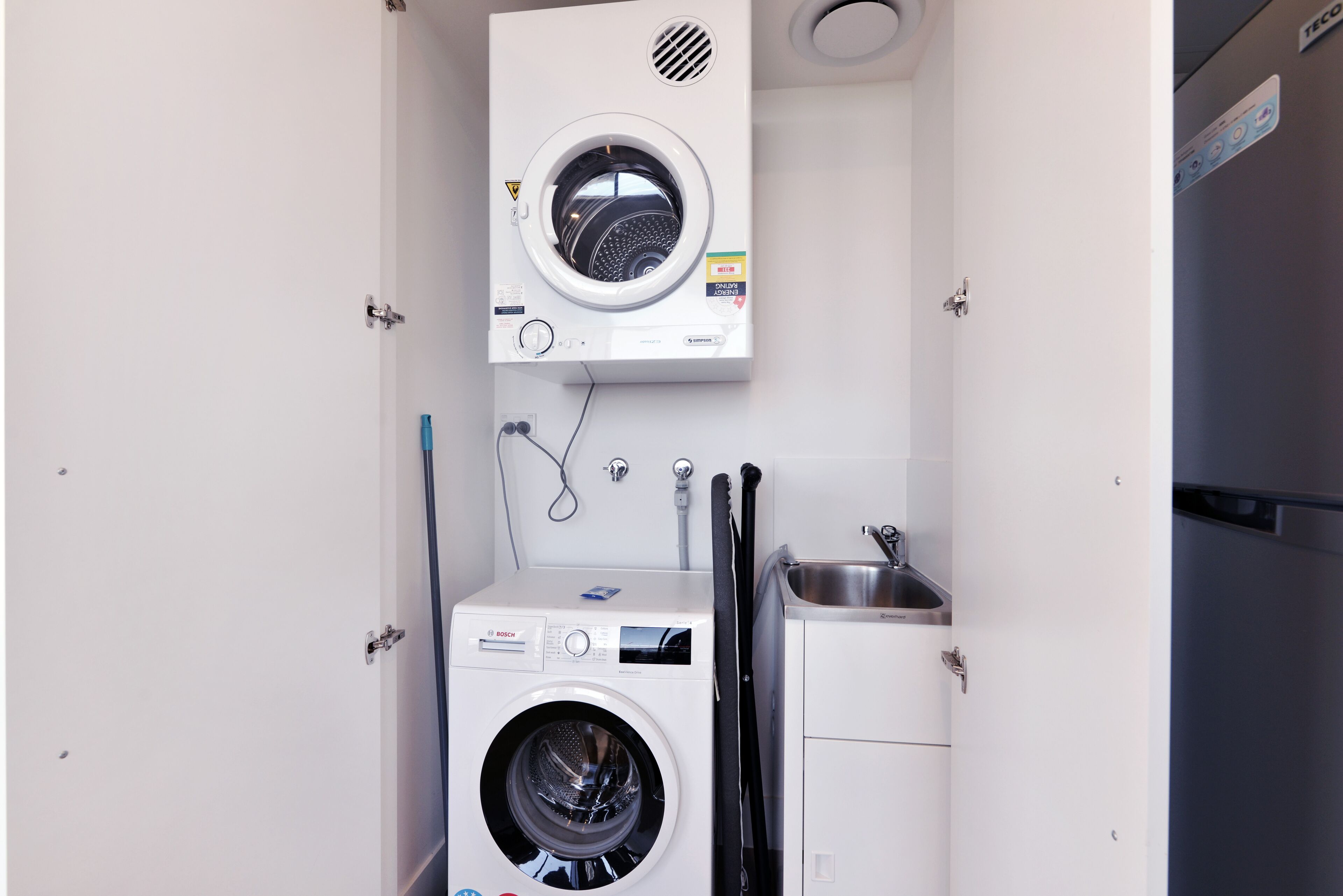 A compact laundry room with a Bosch washing machine, a dryer, and a sink.