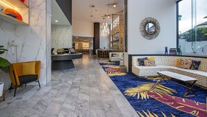 A modern lobby with a marble floor, a reception desk, a sofa with colorful cushions, and a large window offering a view of the outside. - Ruby Gold Coast by CLLIX (Surfers Paradise)