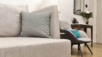 A modern living room with a grey sofa, patterned pillows, a black chair, and a small table with a lamp and a vase of flowers.