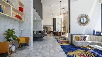 A modern lobby with marble flooring, a reception desk, seating areas, and decorative lighting.