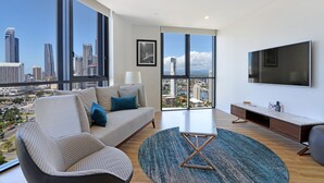A modern living room with a sofa, coffee table, and TV. Large windows offer a city view. - Ruby Gold Coast by CLLIX (Surfers Paradise)