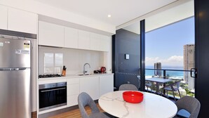 A modern kitchen with a stainless steel refrigerator, a built-in oven, and a dining area with a round table and gray chairs. - Ruby Gold Coast by CLLIX (Surfers Paradise)