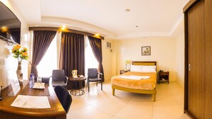 A hotel room with a bed, two chairs, a small table with a pitcher and cups, a desk with a vase of flowers, and a wooden wardrobe. - Rizmy Hotel (Cabuyao)