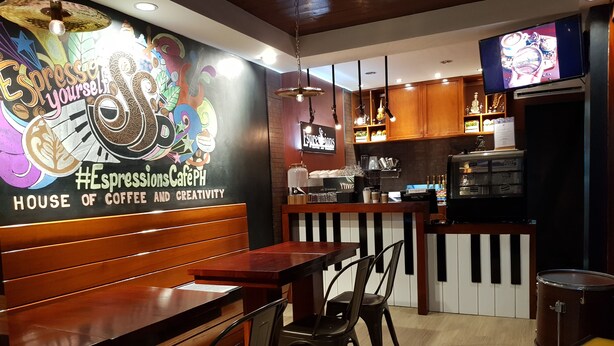 A cozy café with wooden furniture, a mural on the wall, and a television displaying a sports channel. - Rizmy Hotel (Cabuyao)