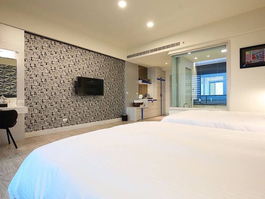Una habitación de hotel moderna con dos camas, televisión, escritorio y baño con ventana grande.