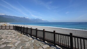 A stone-paved walkway leading to a beach with a wooden fence, overlooking a calm sea and distant mountains. - Seven Stars Sunrise, Seven Stars DEAR (Hualien City)