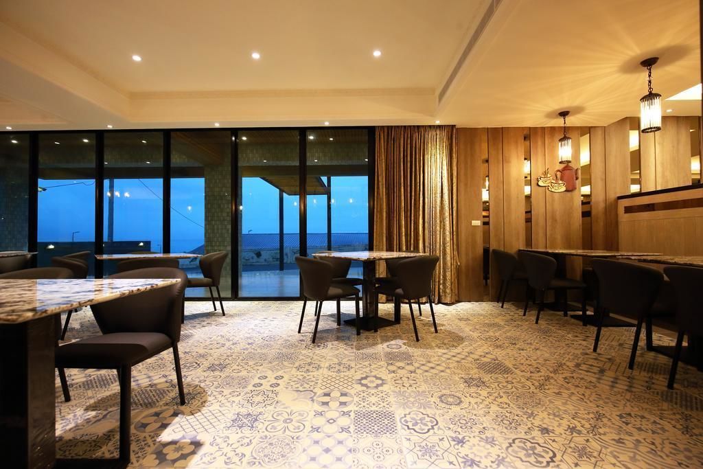 A restaurant with a patterned carpet, tables, chairs, and a view through large windows.