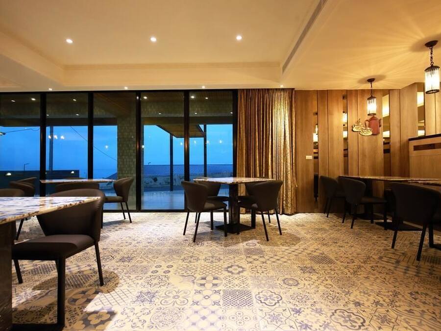 A restaurant with a patterned carpet, tables, chairs, and a view through large windows.