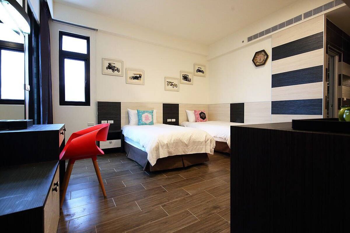 A room with two beds, a desk, and a chair. There are wall decorations and a window.