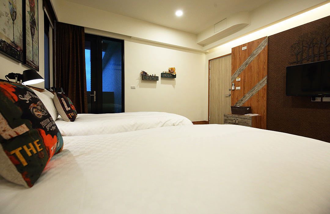 A hotel room with two beds, a television mounted on the wall, and a door leading to the outside.