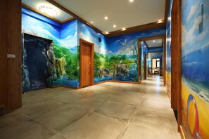 Corredor com um mural retratando uma paisagem natural, incluindo árvores, uma cascata e animais.