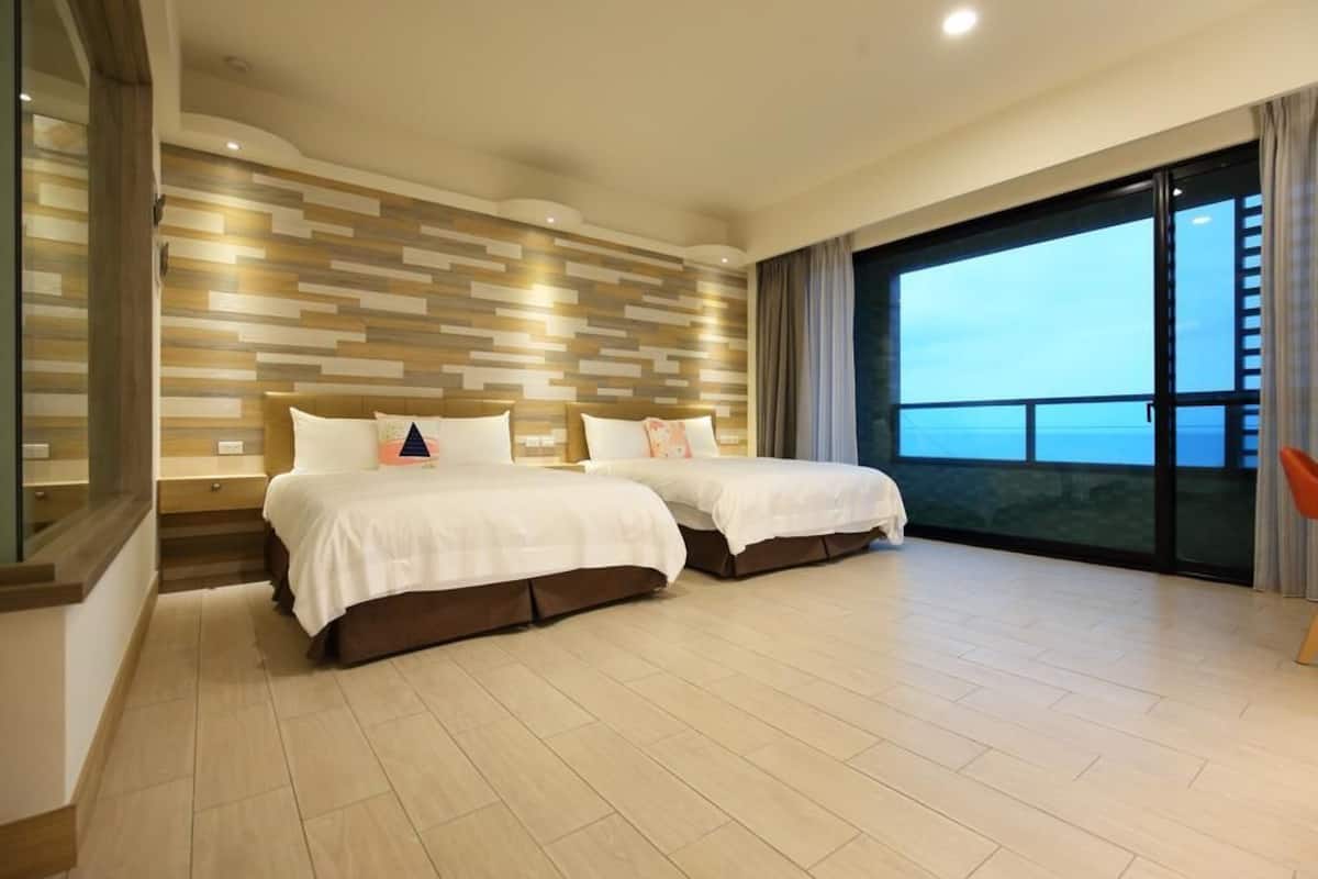 A modern hotel room with two beds, a large window with a view, and a wooden wall design.