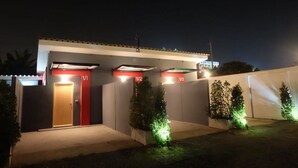 A building with numbered parking bays (VI, V2, V3) and a red door. - Love Box Resort (Bang Phli)