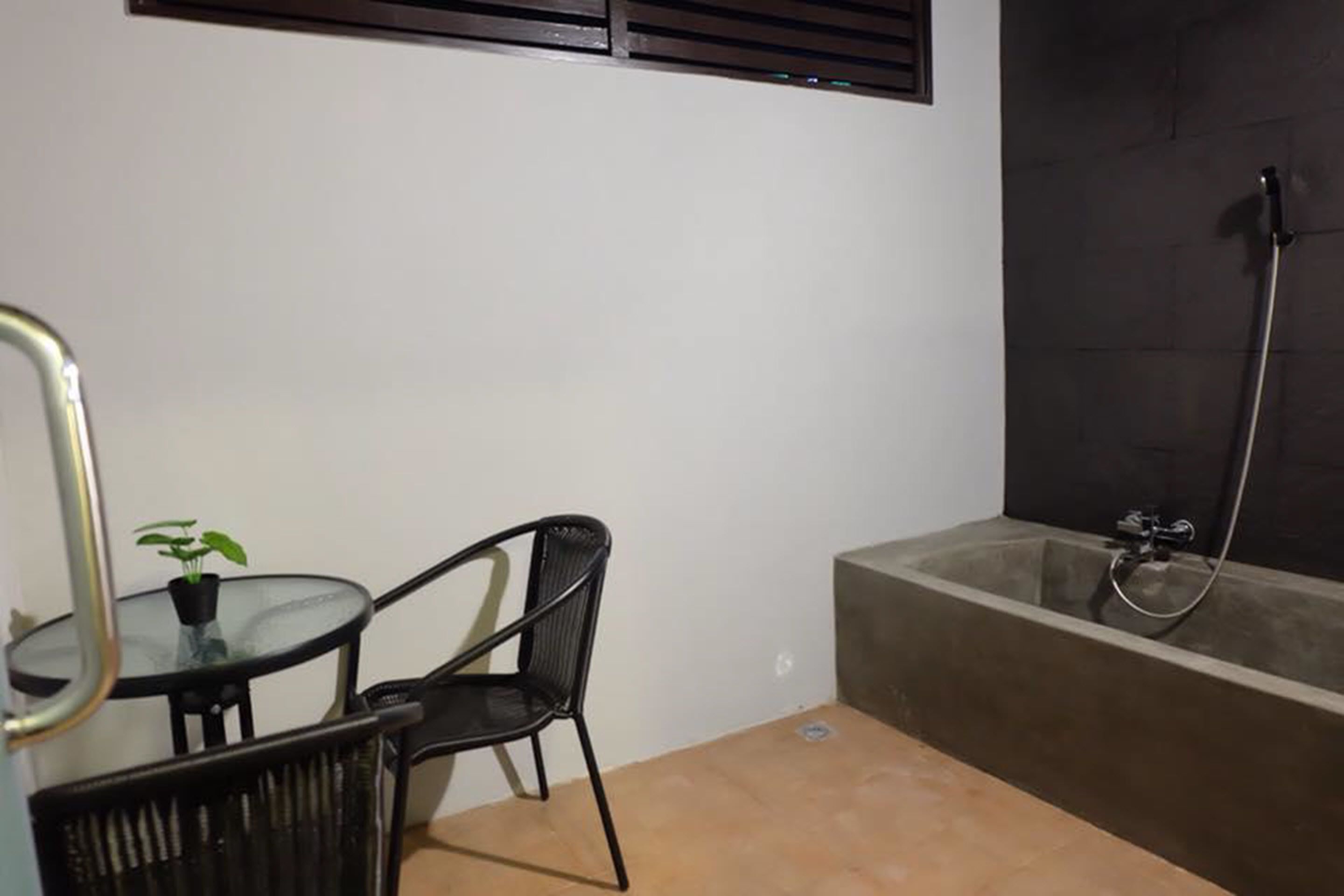 A small, private bathroom with a bathtub, a glass table with a chair, and a potted plant.