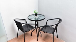 A small round glass table with two black metal chairs, a potted plant on the table, and a white wall in the background. - Love Box Resort (Bang Phli)