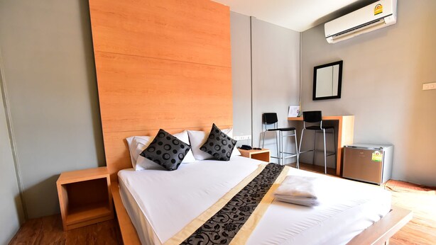 A hotel room with a large bed, a wooden headboard, a desk with a chair, and a small refrigerator. - Love Box Resort (Bang Phli)