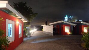 A hotel entrance with a red facade, multiple rooms with white walls, and a gravel pathway. - Love Box Resort (Bang Phli)