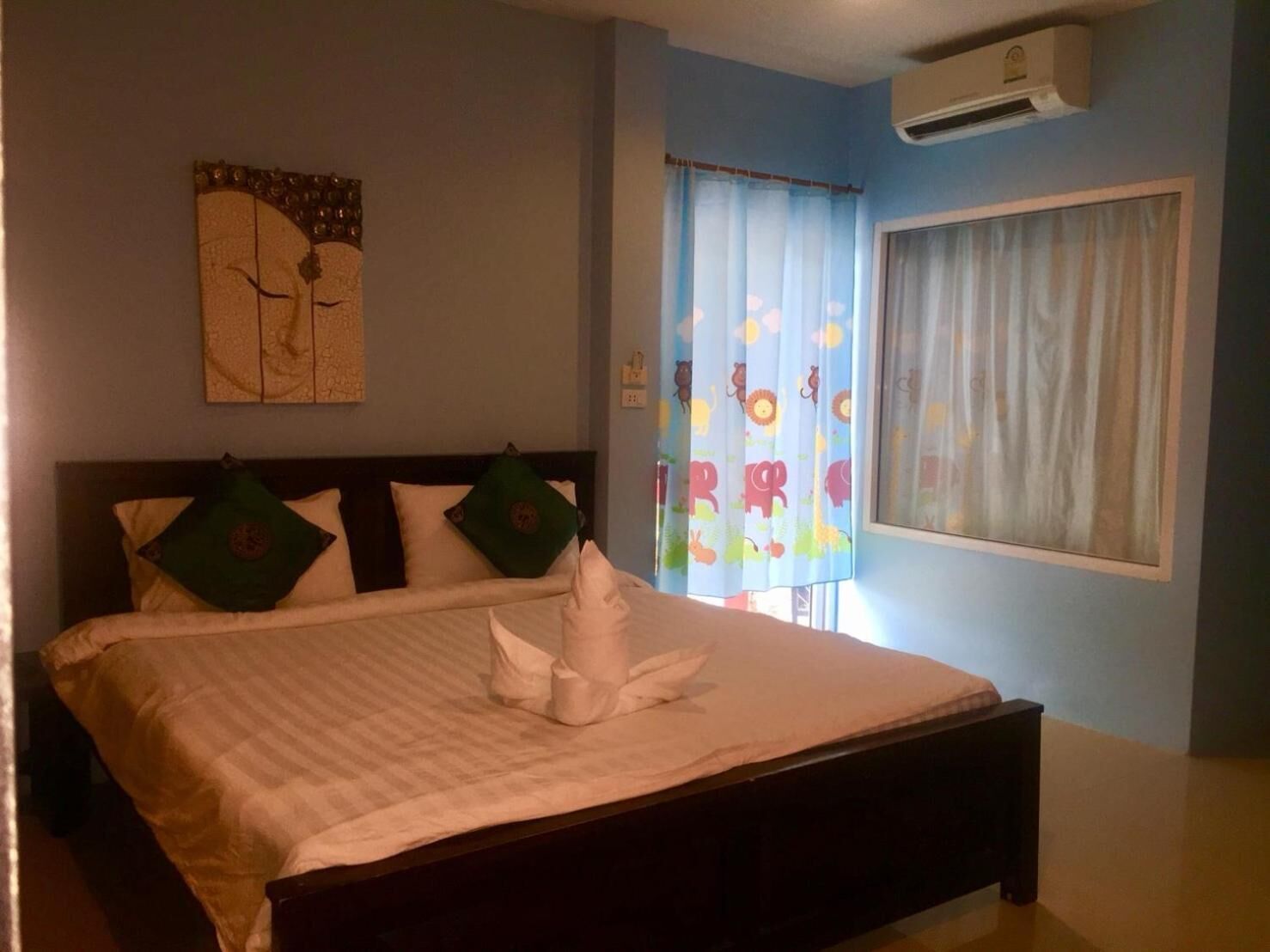 A bedroom with a bed, a wall-mounted air conditioner, a window with curtains, and a wall decoration.