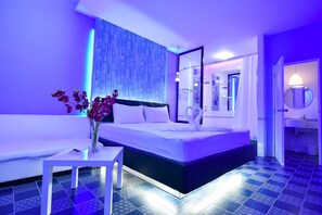 A modern hotel room with a large bed, a white sofa, a small table, and a bathroom visible through an open door. - Relax Villa Hotel (Samut Prakan)