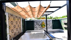 A modern outdoor spa area with a large bathtub, a pergola providing shade, and decorative wall panels. - Relax Villa Hotel (Samut Prakan)