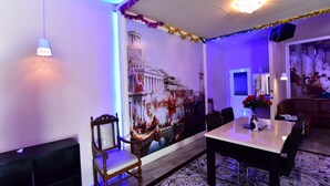 A dining area with a mural of a historical building, a chandelier, and a table with chairs. - Relax Villa Hotel (Samut Prakan)