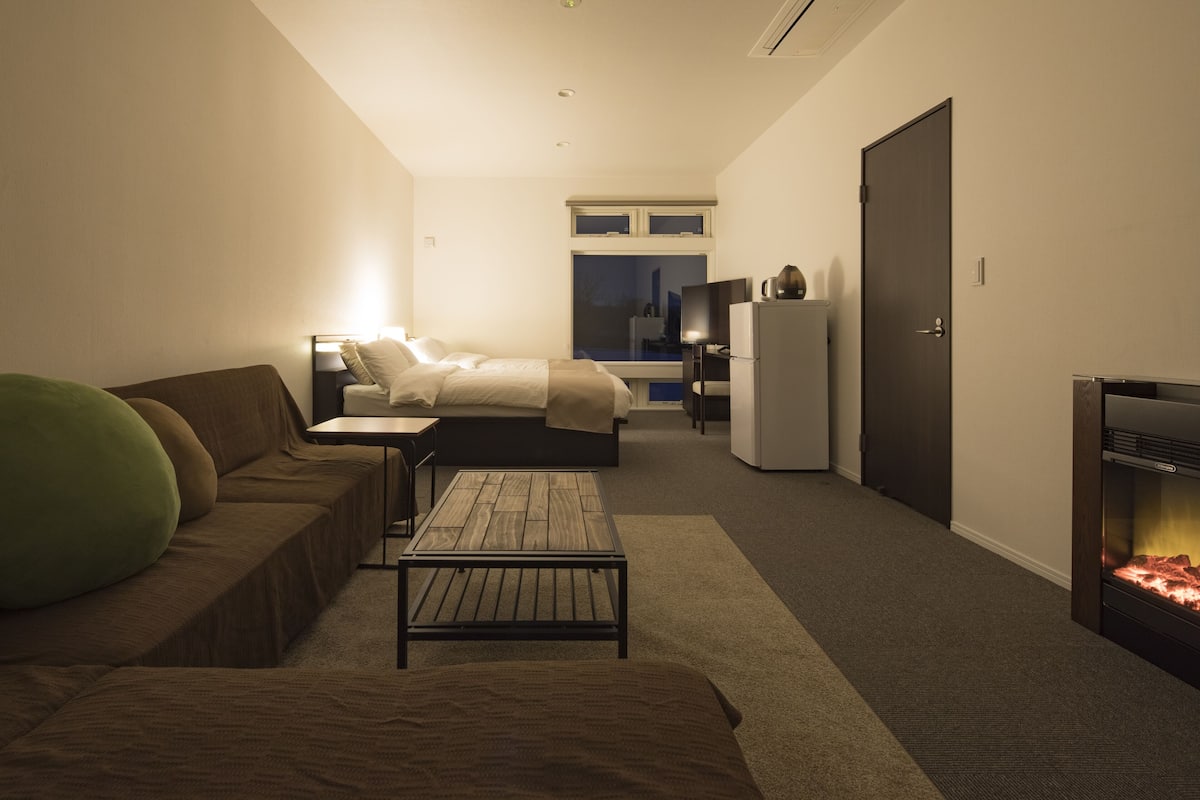 Ein modernes Hotelzimmer mit einer Couch, einem kleinen Tisch, einem Bett, einem Fernseher, einem Kühlschrank und einem Kamin.