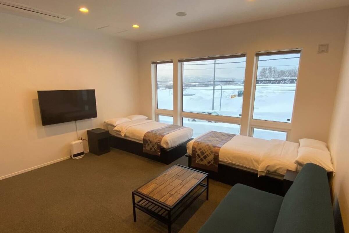 Ein Zimmer mit zwei Betten, einem Sofa, einem Fernseher und großen Fenstern mit Blick auf Schnee.