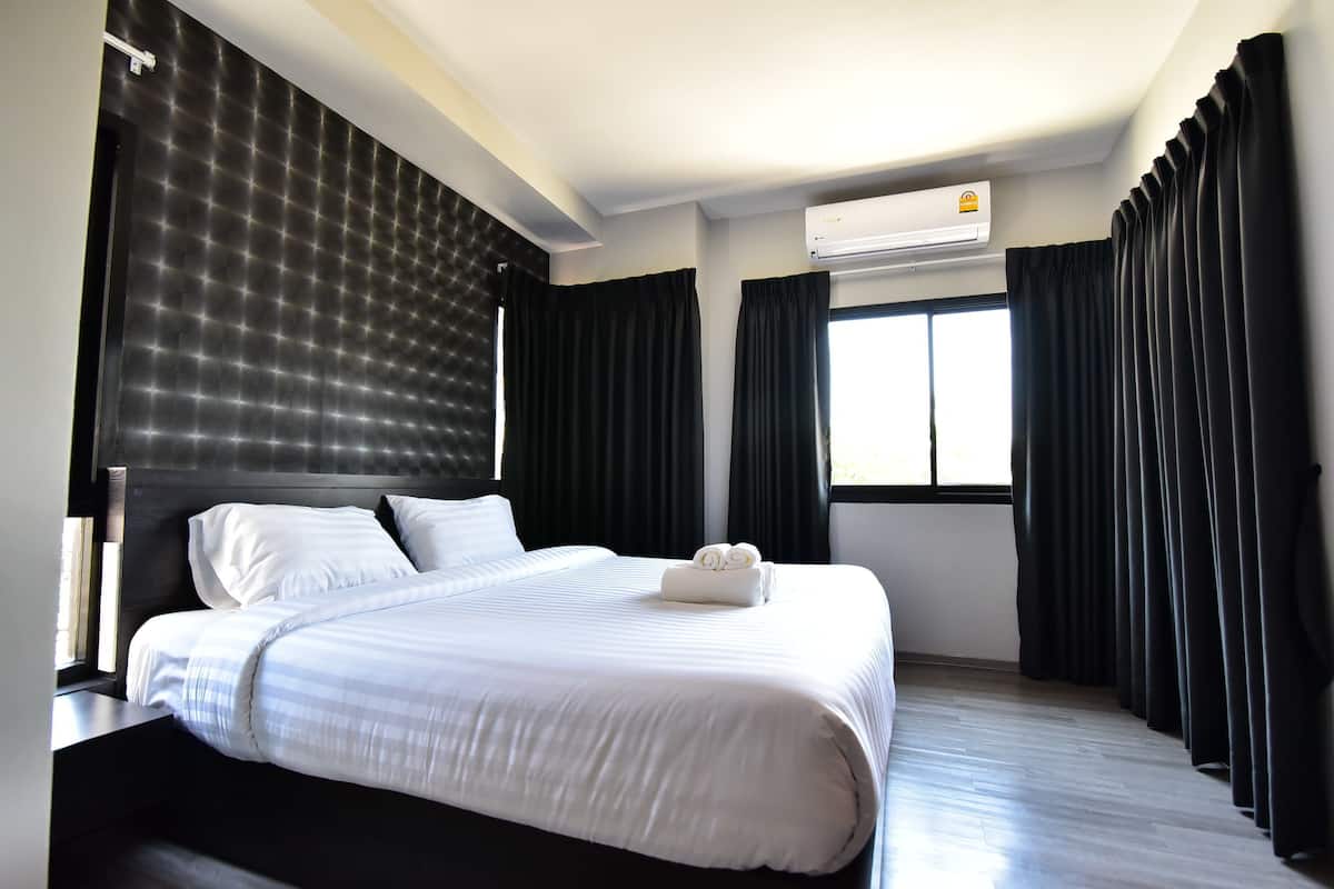 Une chambre d’hôtel moderne avec un grand lit, des rideaux foncés et un appareil de climatisation.
