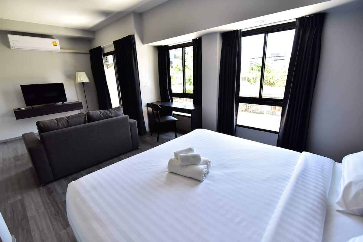 Une chambre d’hôtel avec un lit, un canapé, un bureau, une télévision et une fenêtre avec des rideaux.