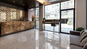 A modern reception area with a marble counter, a large window offering a view of the street, and a sofa with patterned cushions. - At S115 Residence (Samut Prakan)