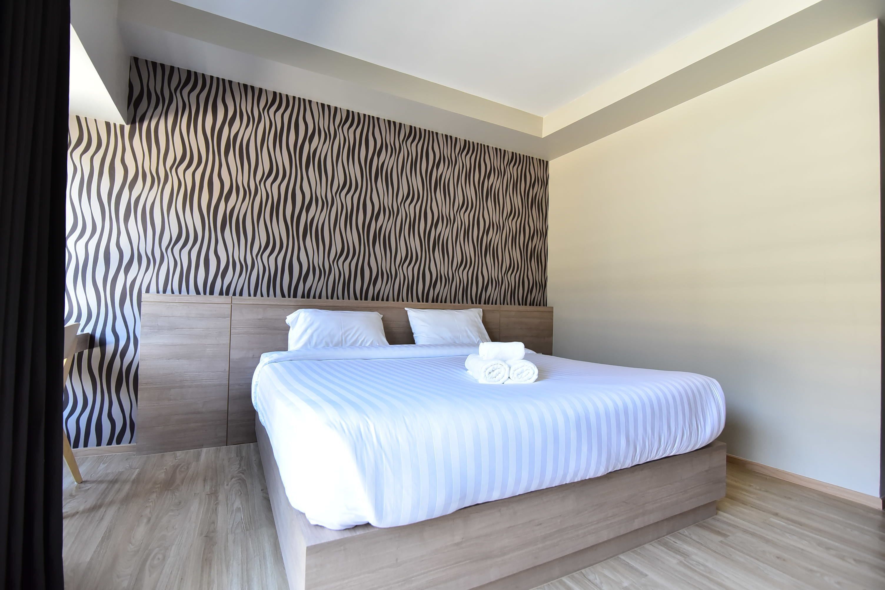 Una habitación de hotel moderna con una cama grande, cabecera de madera y pared con un diseño ondulado.