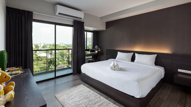A modern hotel room with a large bed, a desk with a laptop, and a view of the city through large windows. - At S115 Residence (Samut Prakan)