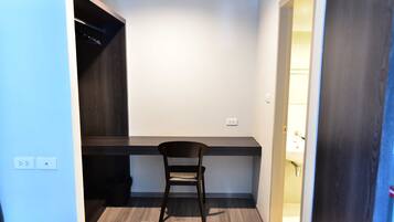 A small, modern room with a dark wood floor, a single dark wooden chair, a built-in desk, and a white wall.